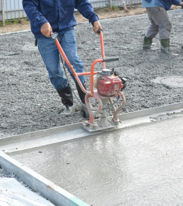 Team of construction workers using power tools to level freshly poured concrete on a building site.